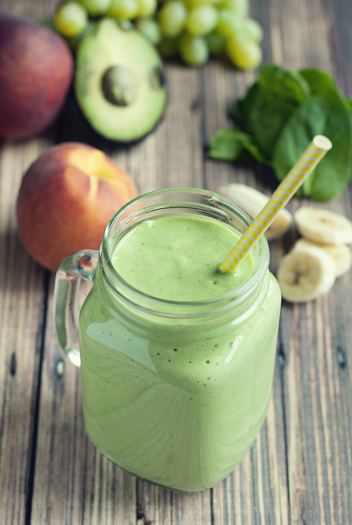 banana peach green smoothie in a clear jar with fresh ingredients behind it