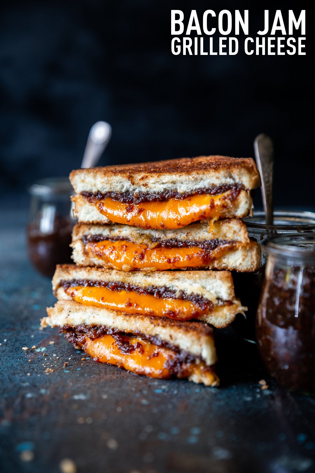 Bacon jam in small tulip jars, spoon with bacon jam on it, bacon jam grilled cheese triangles stacked on each other