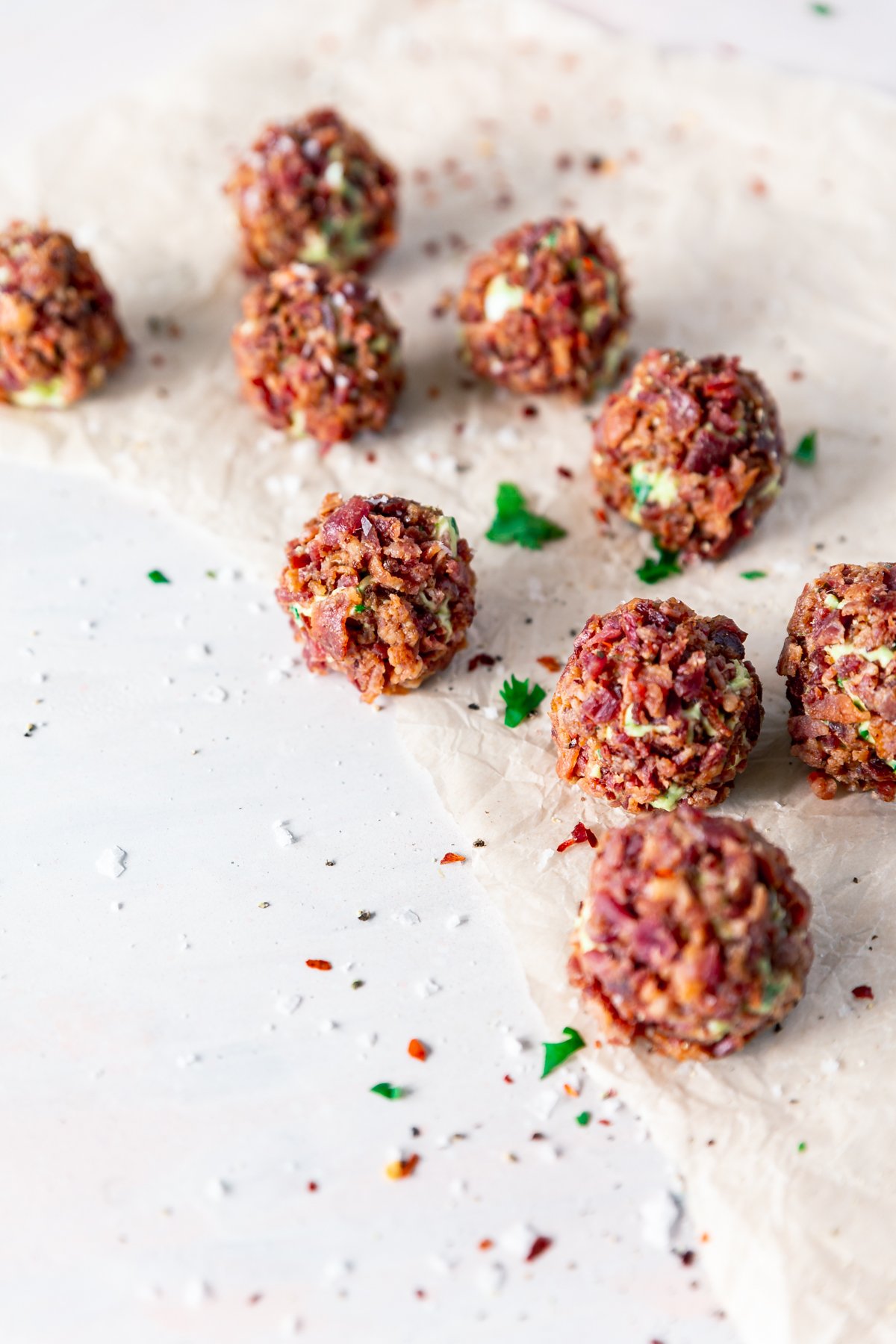 angled view of fat bomb balls covered with bits of crispy bacon, showing some avocado between pieces, surrounded in a sprinkling of salt, pepper, red pepper flakes, and cilantro