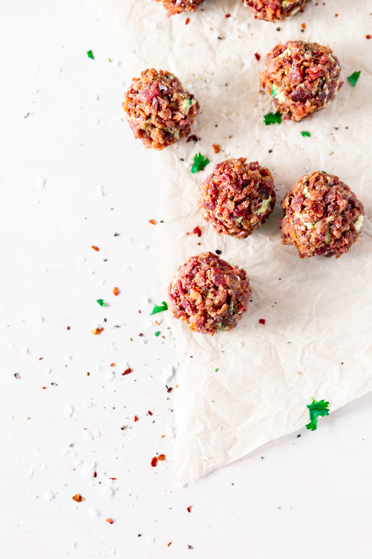 overhead view of fat bomb balls covered with bits of crispy bacon, showing some avocado between pieces, surrounded in a sprinkling of salt, pepper, red pepper flakes, and cilantro
