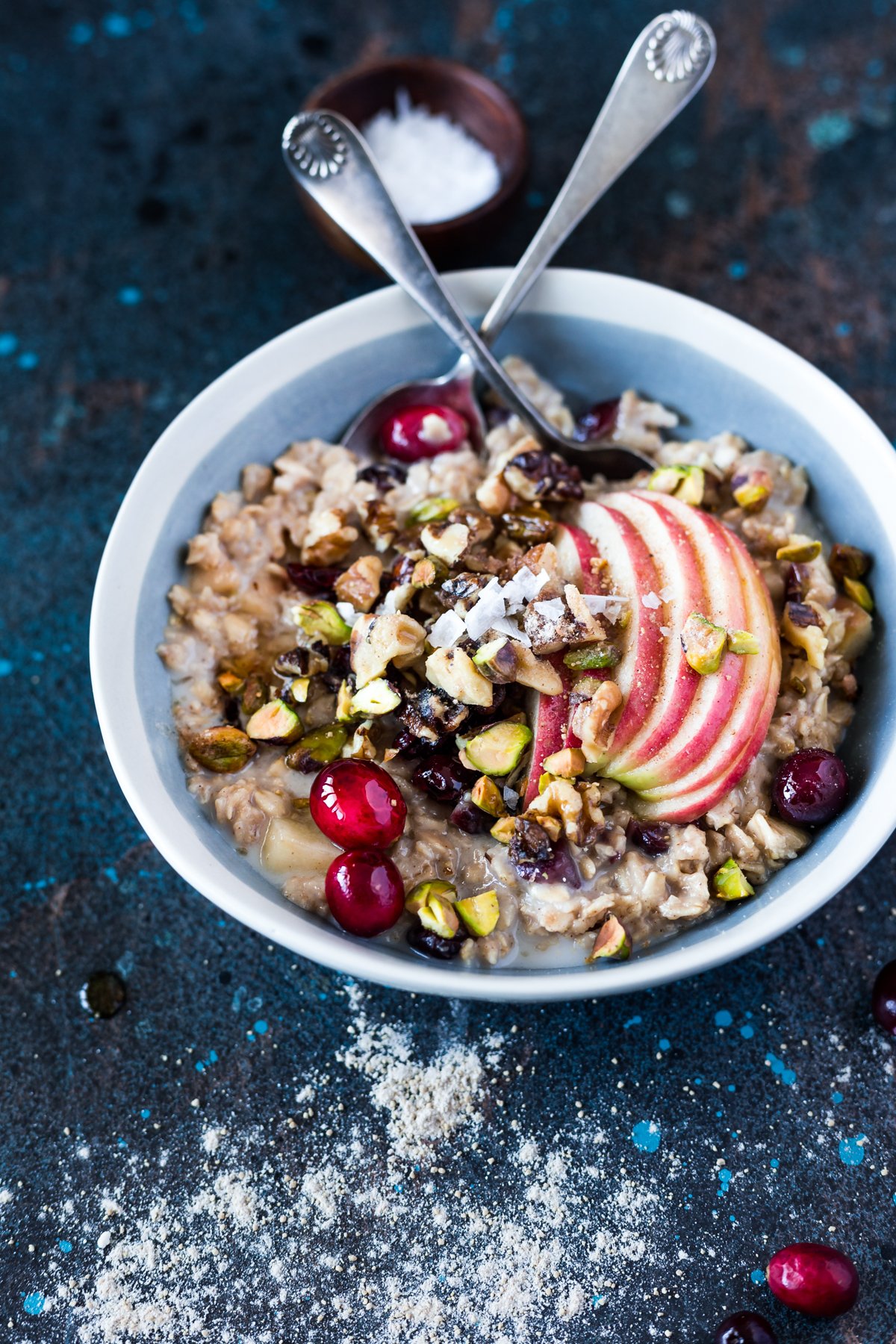 bowl of slow cooker warm apple and cranberry overnight oats topped with sliced apple, pistachios, walnuts, and fresh cranberries