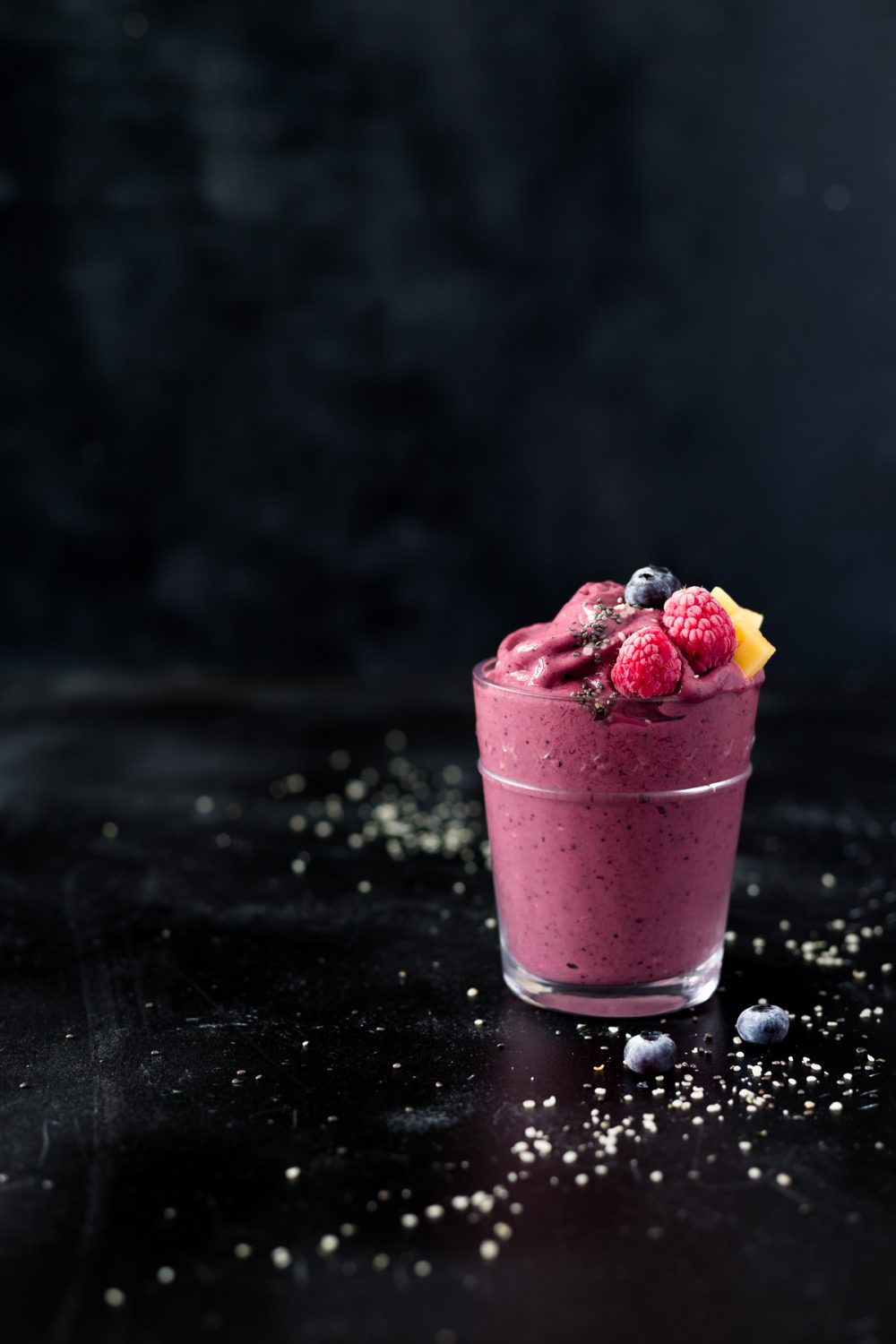 glass with mango berry tropical smoothie topped with fresh frozen berries, mango, hemp hearts and chia seeds