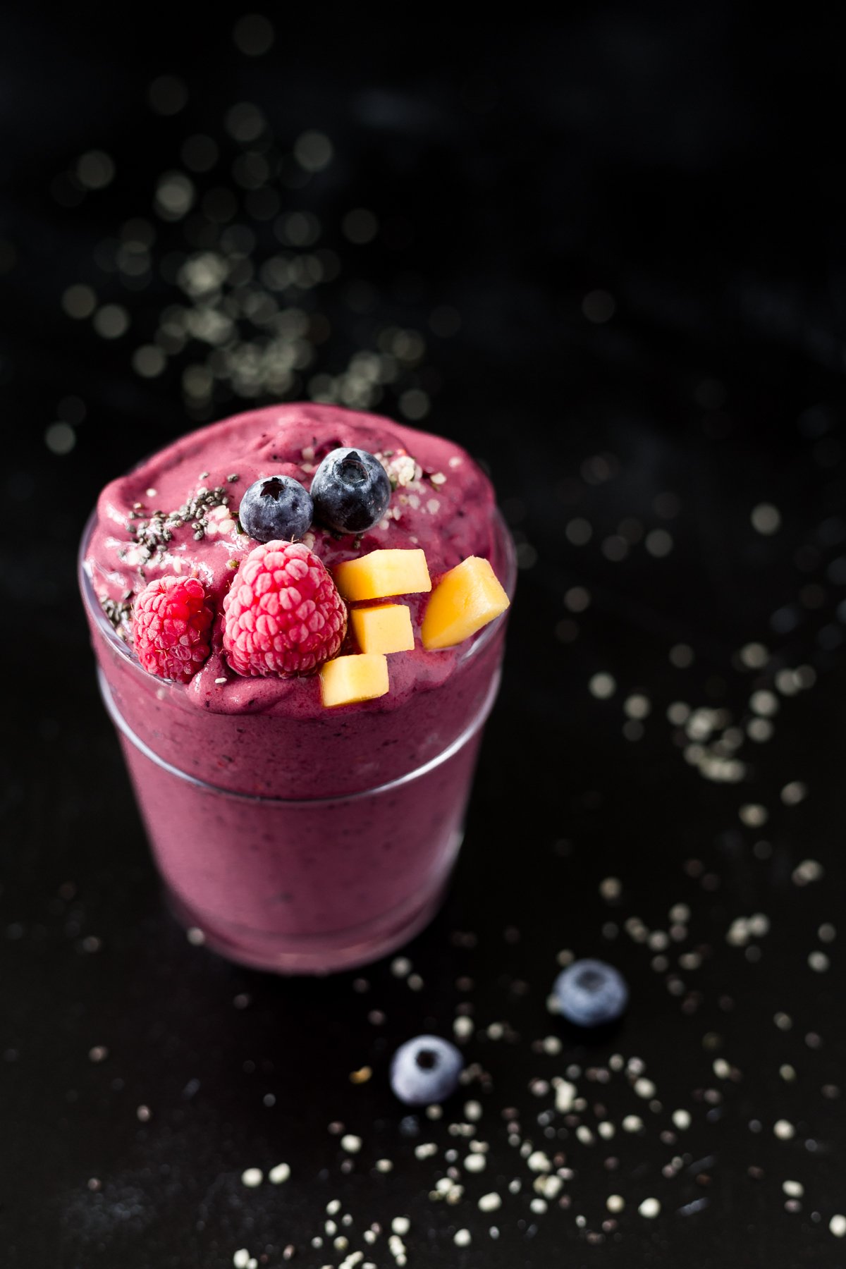 glass with mango berry tropical smoothie topped with fresh frozen berries, mango, hemp hearts and chia seeds