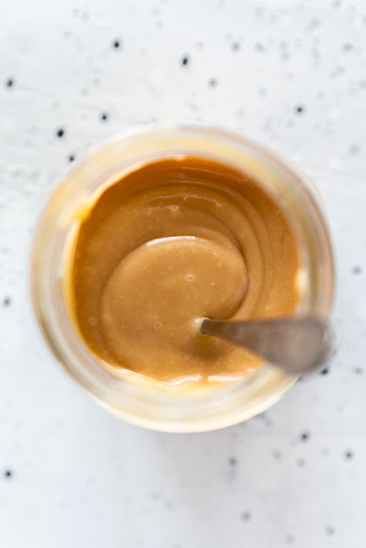 overhead view of a jar of dulce de leche with a spoon inside.