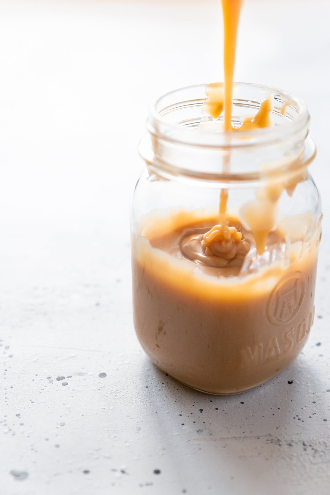 forty-five degree angled shot of a jar of dulce de leche, with a rivulet of caramel pouring into the jar.