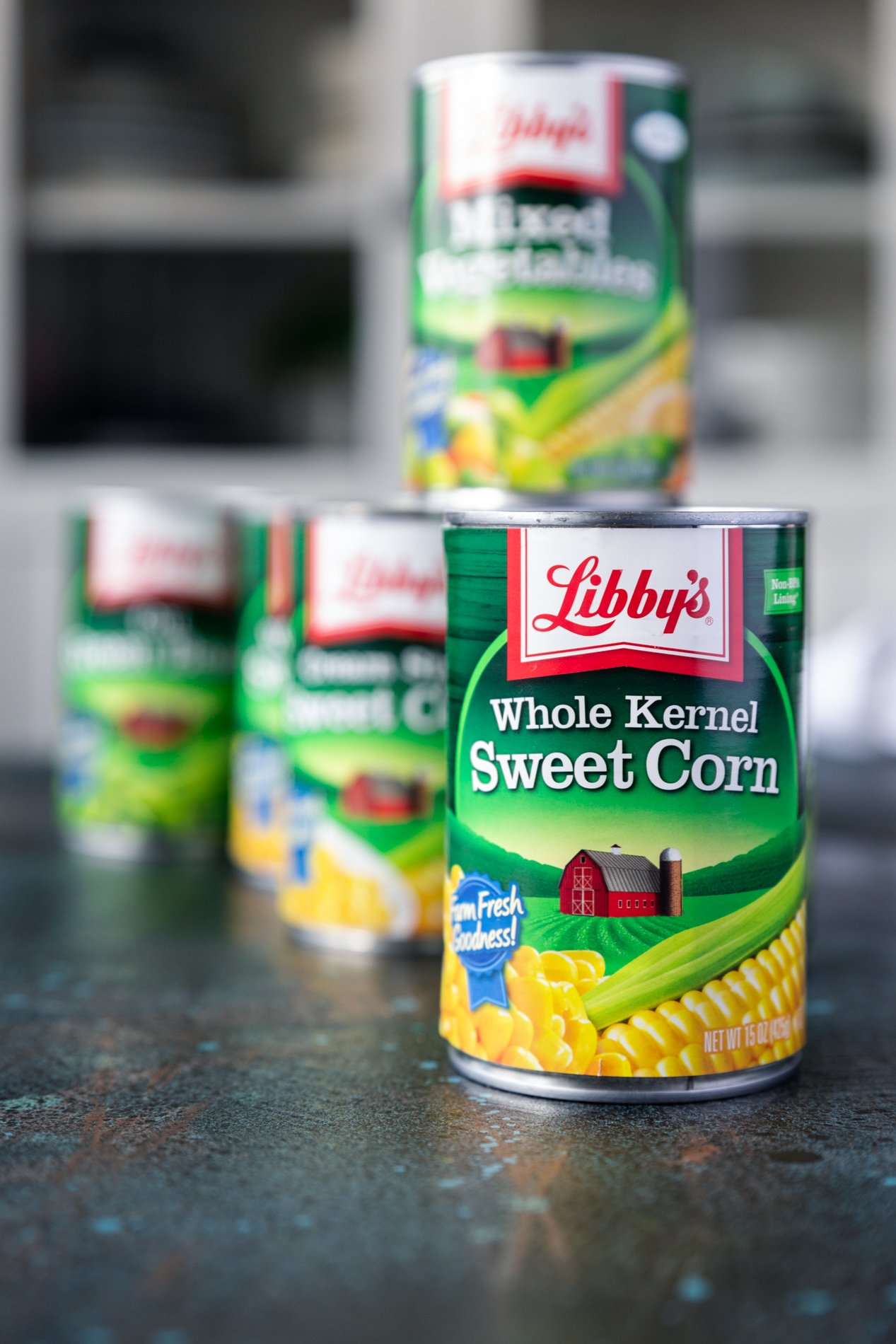 a straight-forward shot of canned vegetables, with a can of corn in sharp focus in front and several blurred cans behind it, one of which is stacked.