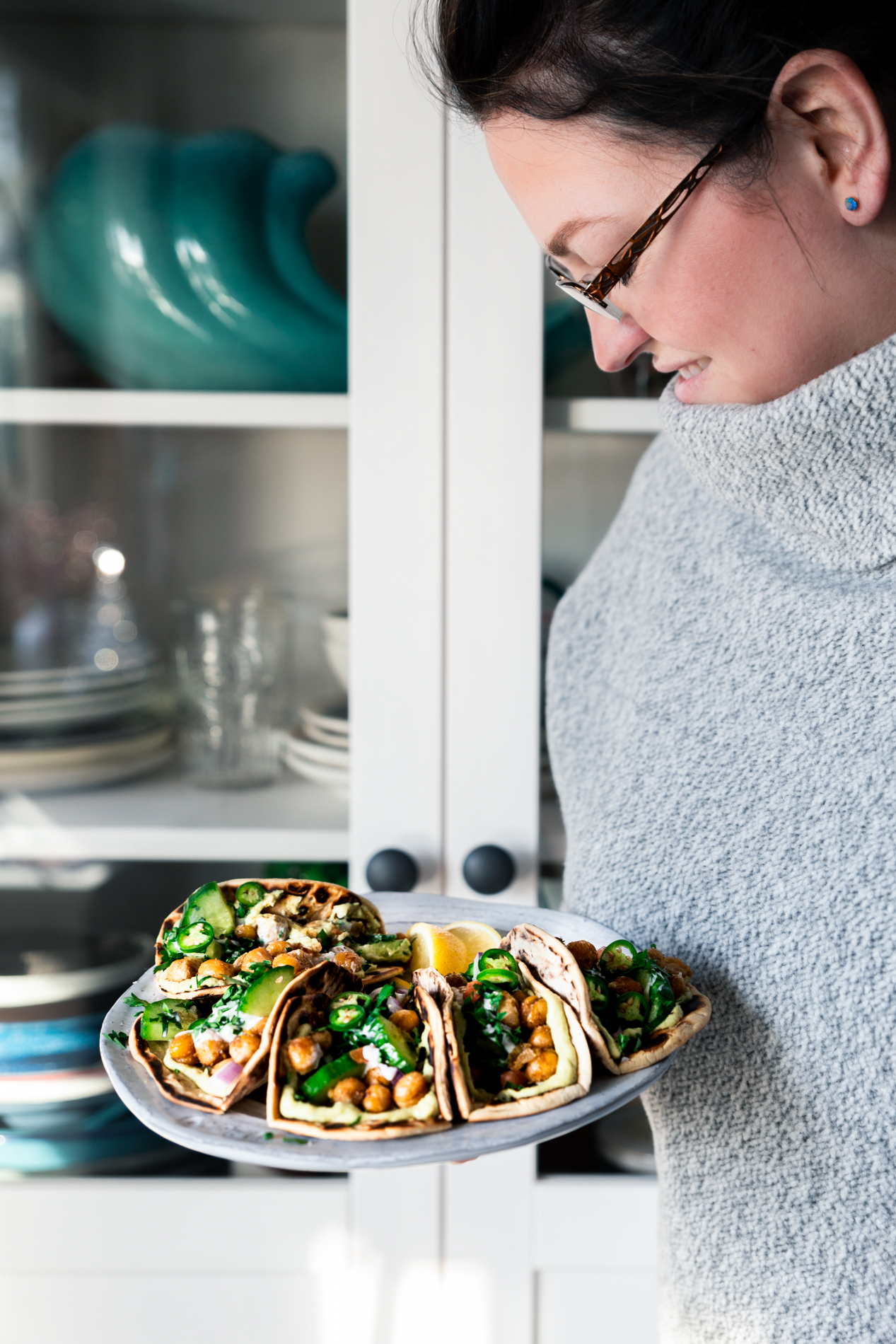 straight forward view of a woman holding a plate of deconstructed falafel pita tacos.