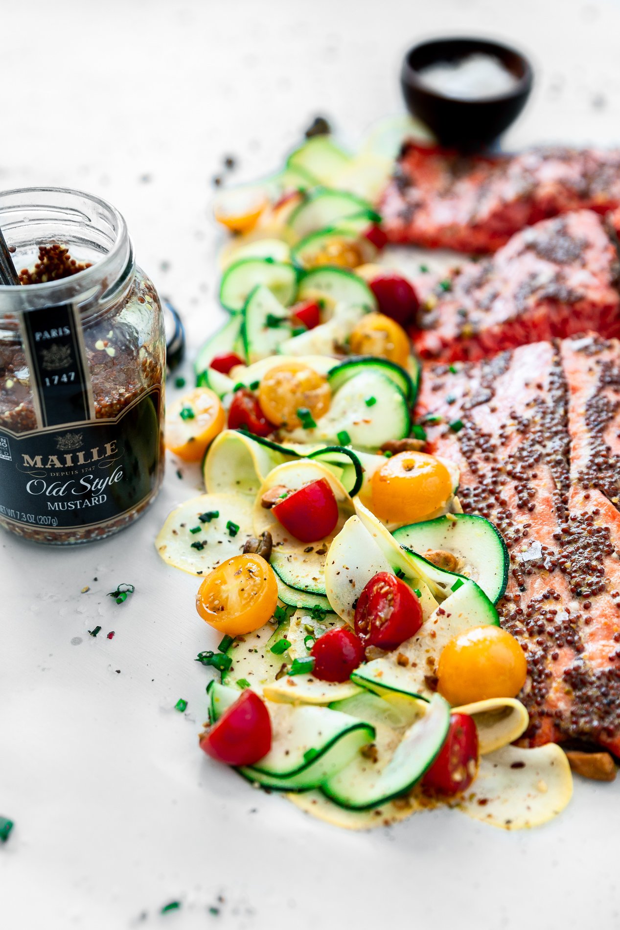 side angled view of mustard salmon with citrus squash salad and an open jar of maille mustard