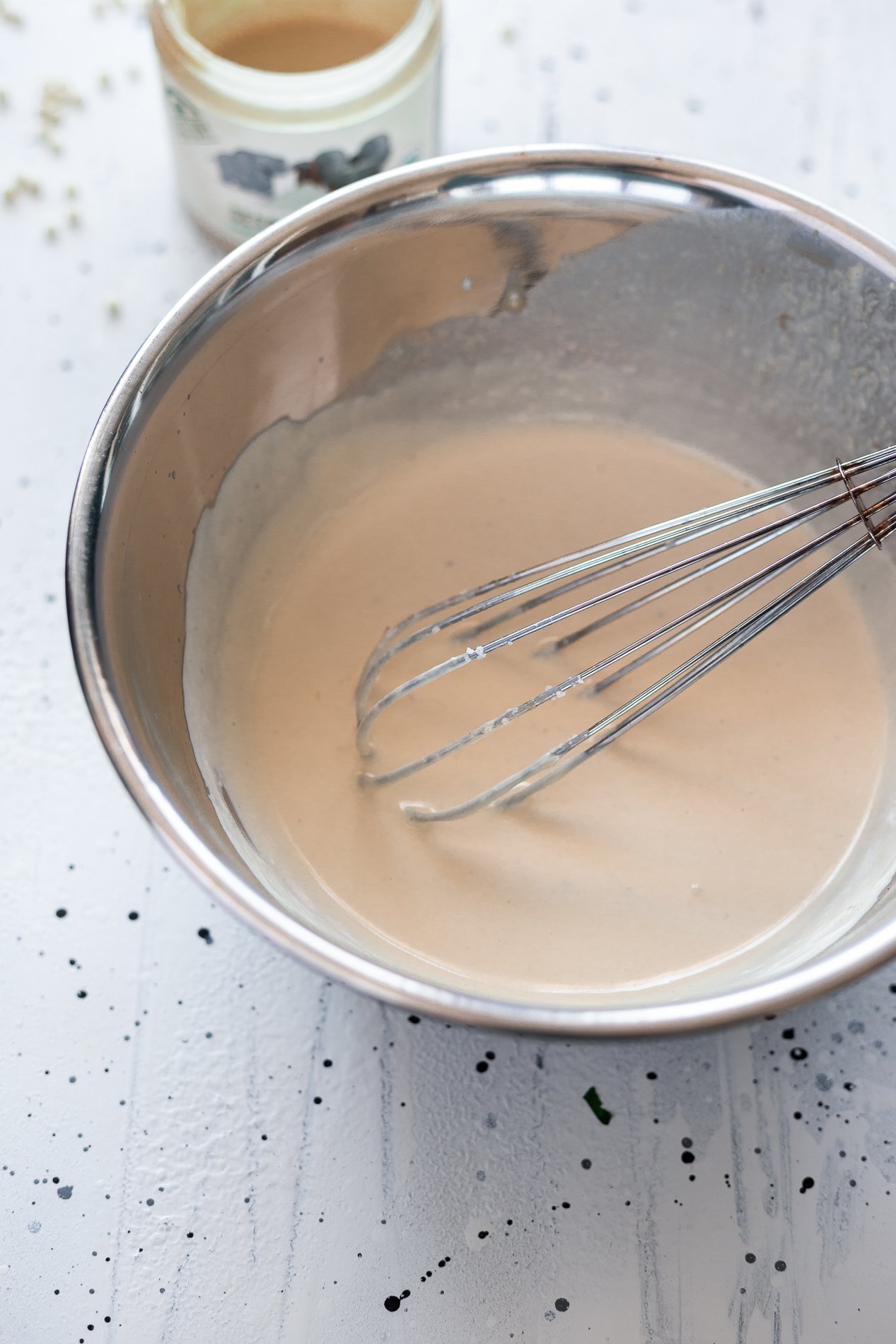 slightly angled view of a bowl of lemon tahini dressing with a whisk inside it