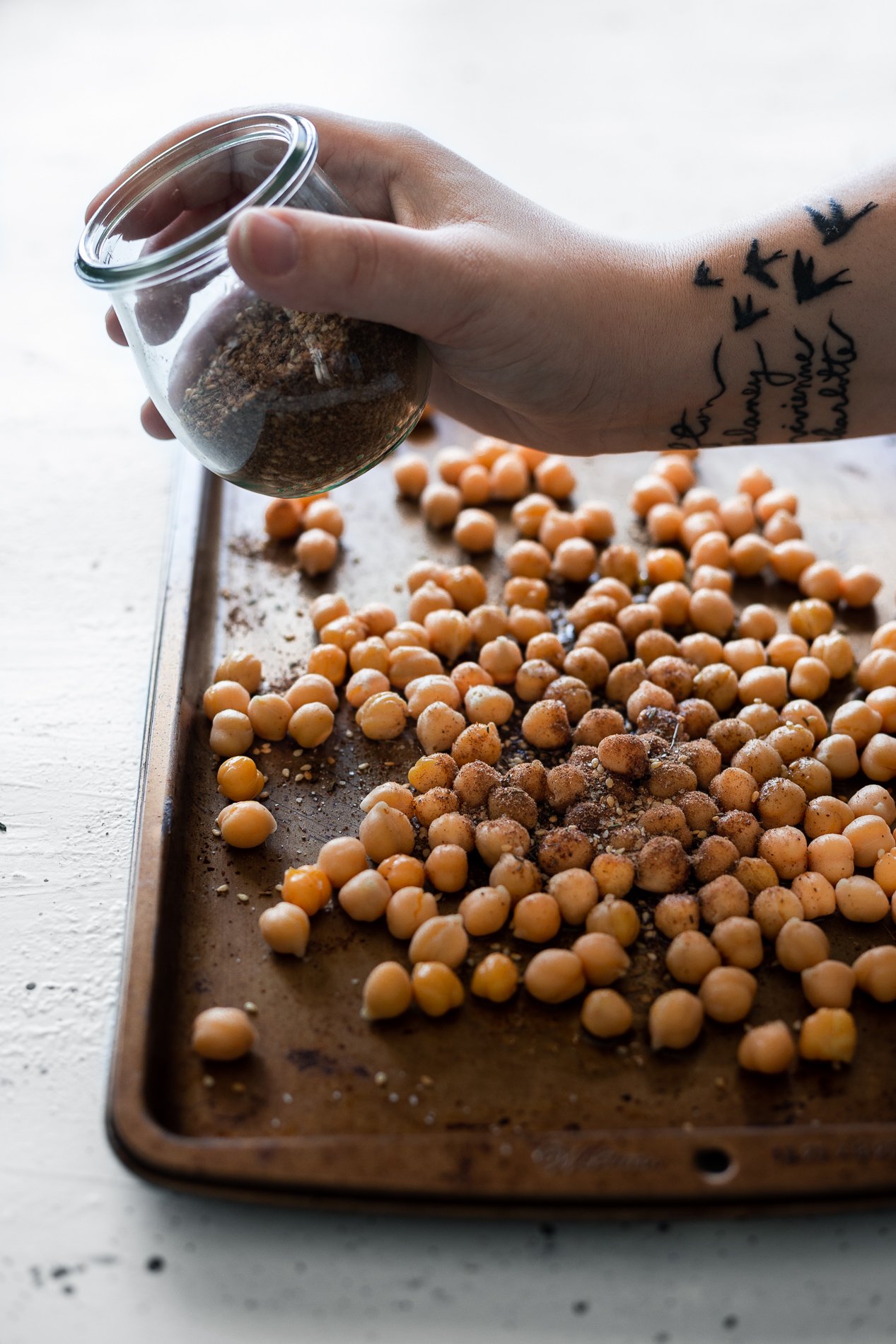 side view of an arm sprinkling za'atar seasoning over chickpeas on a baking sheet