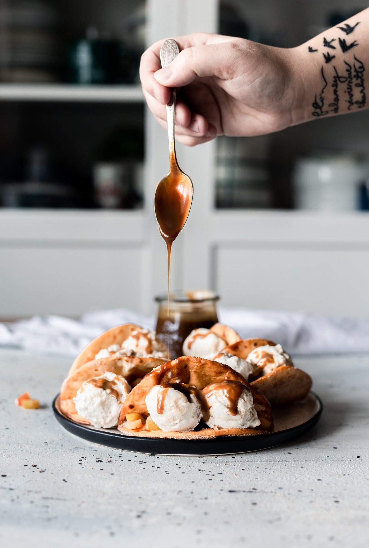 a hand drizzling vegan caramel sauce onto a plate of easy apple crumble dessert tacos