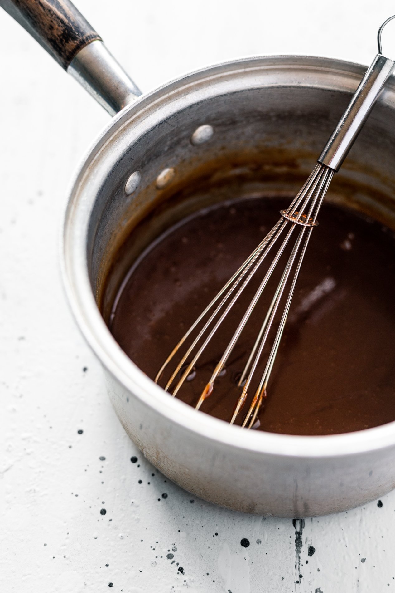 angled view of a pot of vegan caramel sauce after cooking down, with a whisk inside the pot