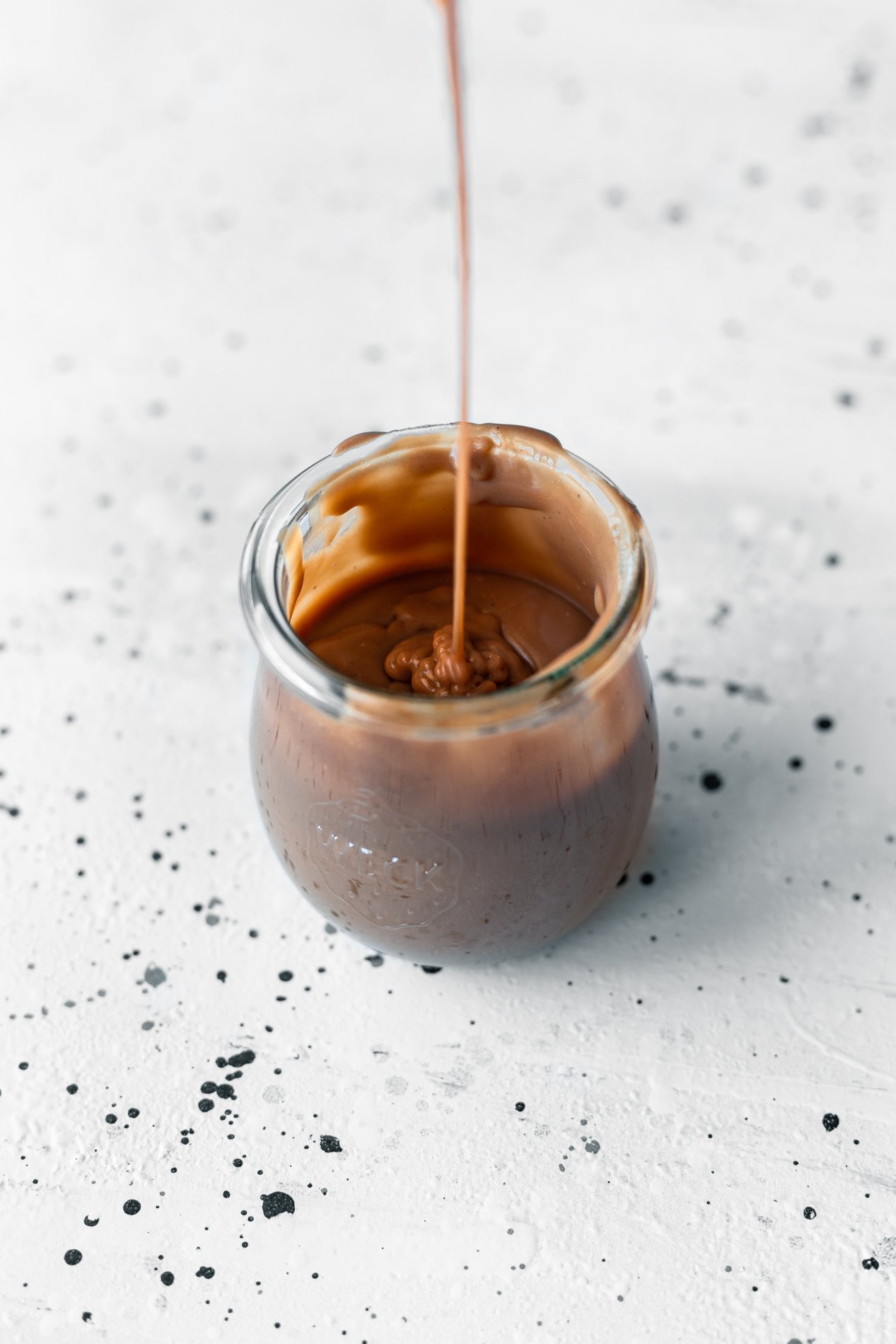 angled view of a small jar of vegan caramel sauce with a drizzle pouring into the jar