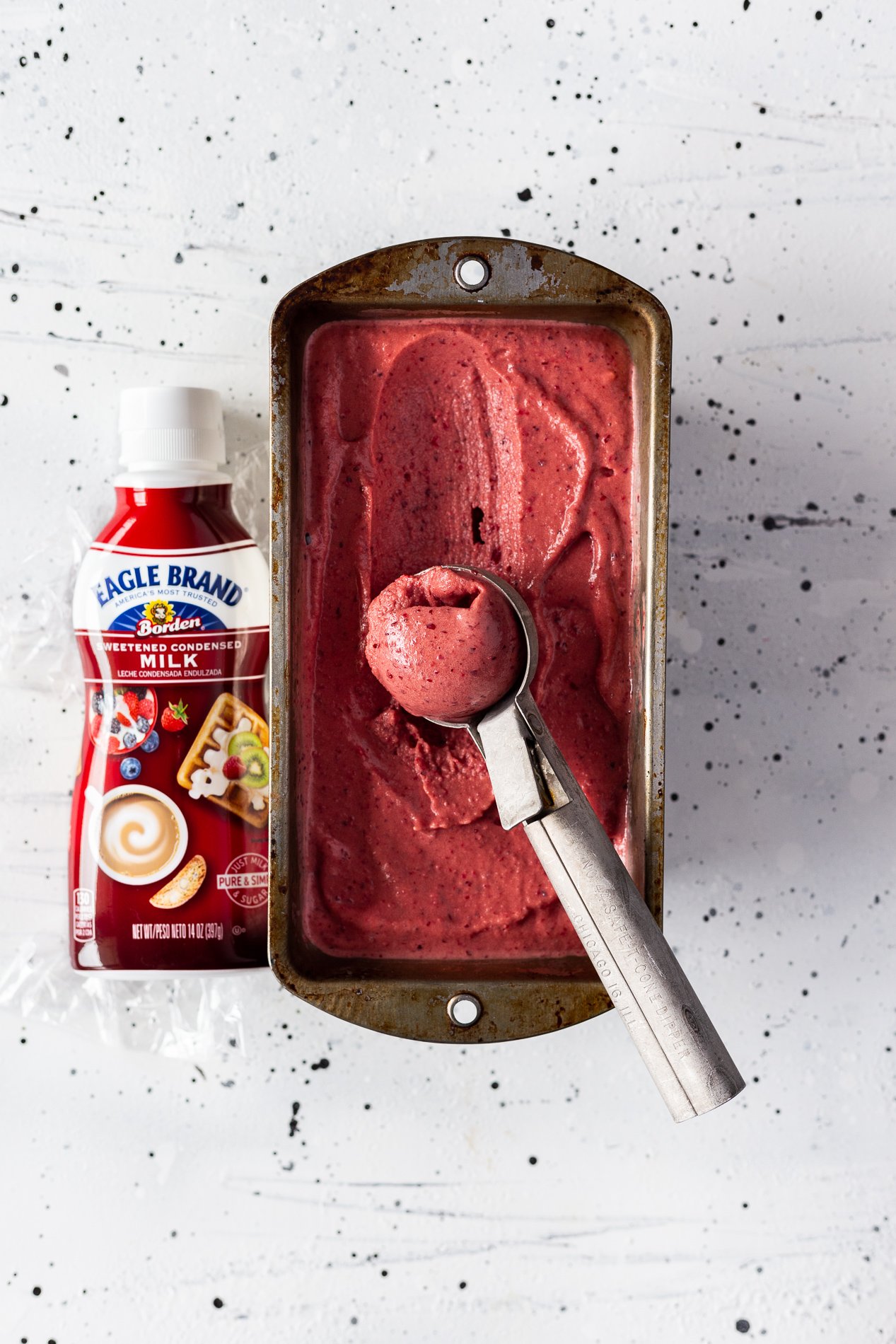 overhead view of a tin of instant cherry ice cream with a scoop taken out of it and a bottle of sweetened condensed milk beside it