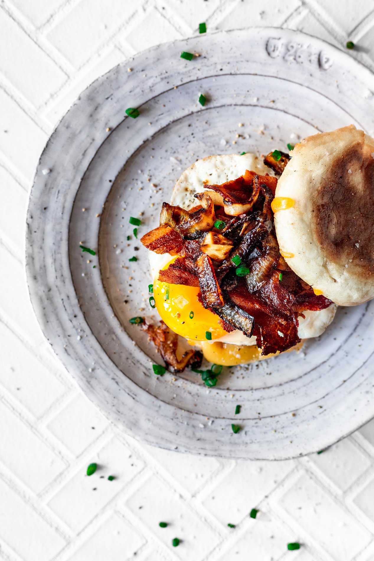 overhead view of maple bacon english muffin breakfast burger on a white plate with scattered chives