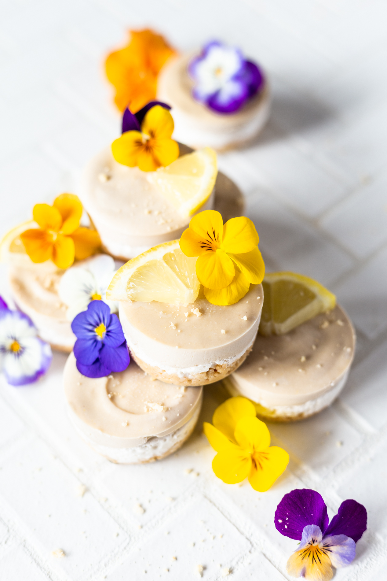 angled view of eight mini lemon vegan cheesecakes with lemon slices and fresh edible flowers