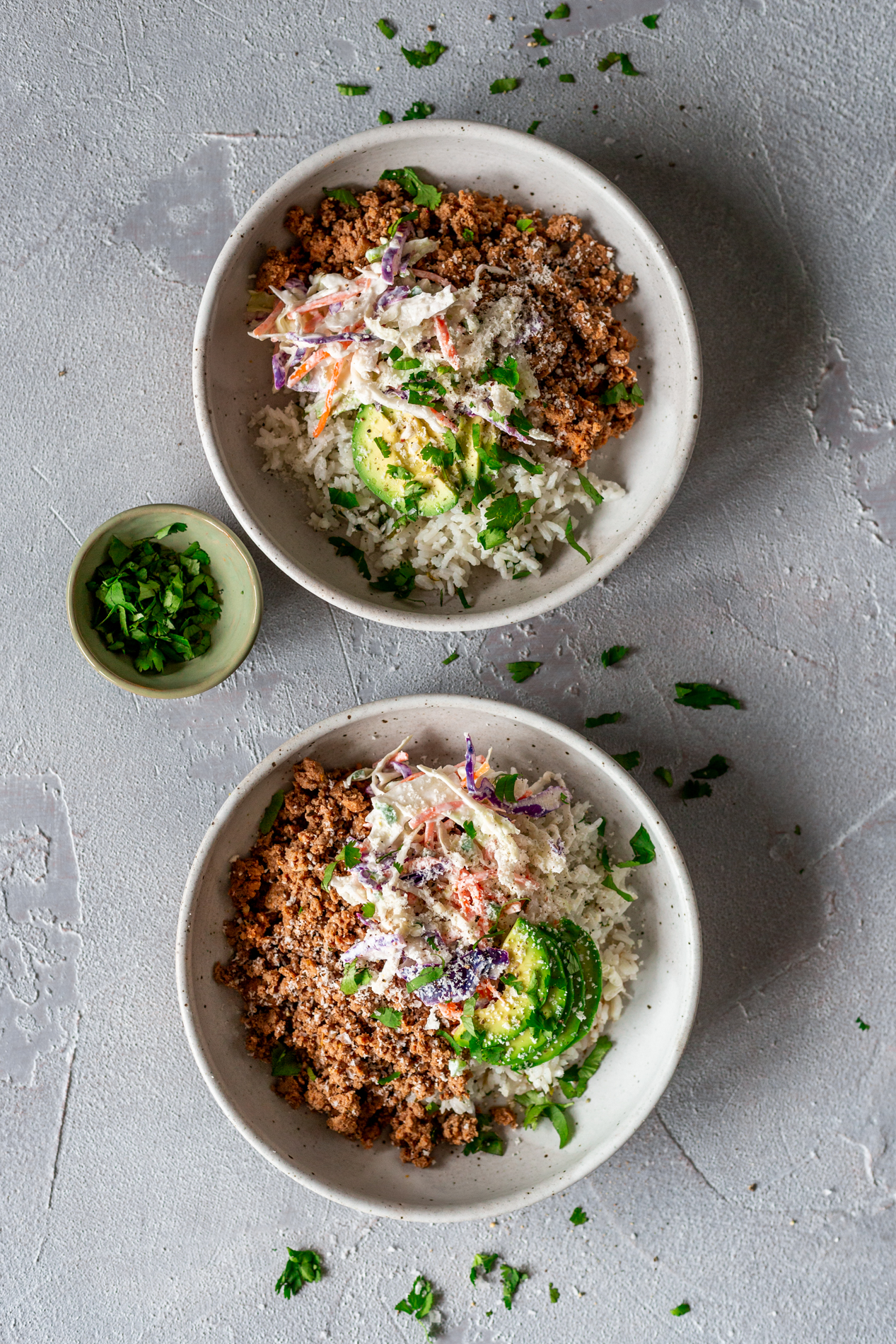 overhead view of two burrito bowls lined up vertically in-image, with a small bowl of cilantro beside them
