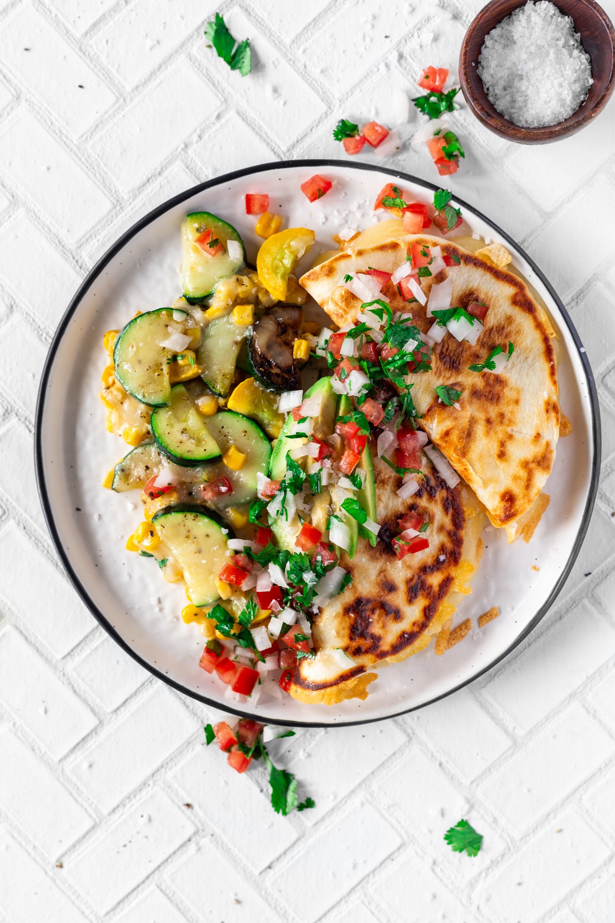 overhead view of a plate with calabacitas con elote, or zucchini with corn, plated with quesadillas, pico de gallo, and avocado