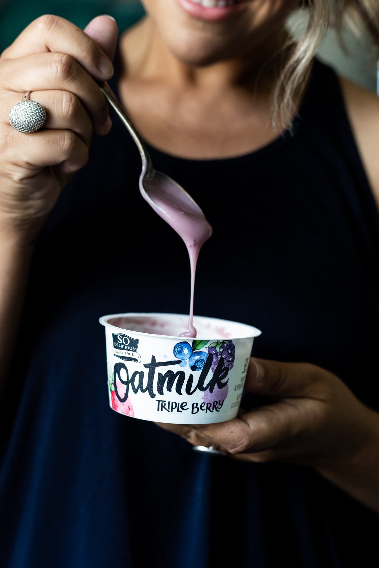 food blogger karly gomez holding a container of so delicious dairy free triple berry oatmilk yogurt alternative
