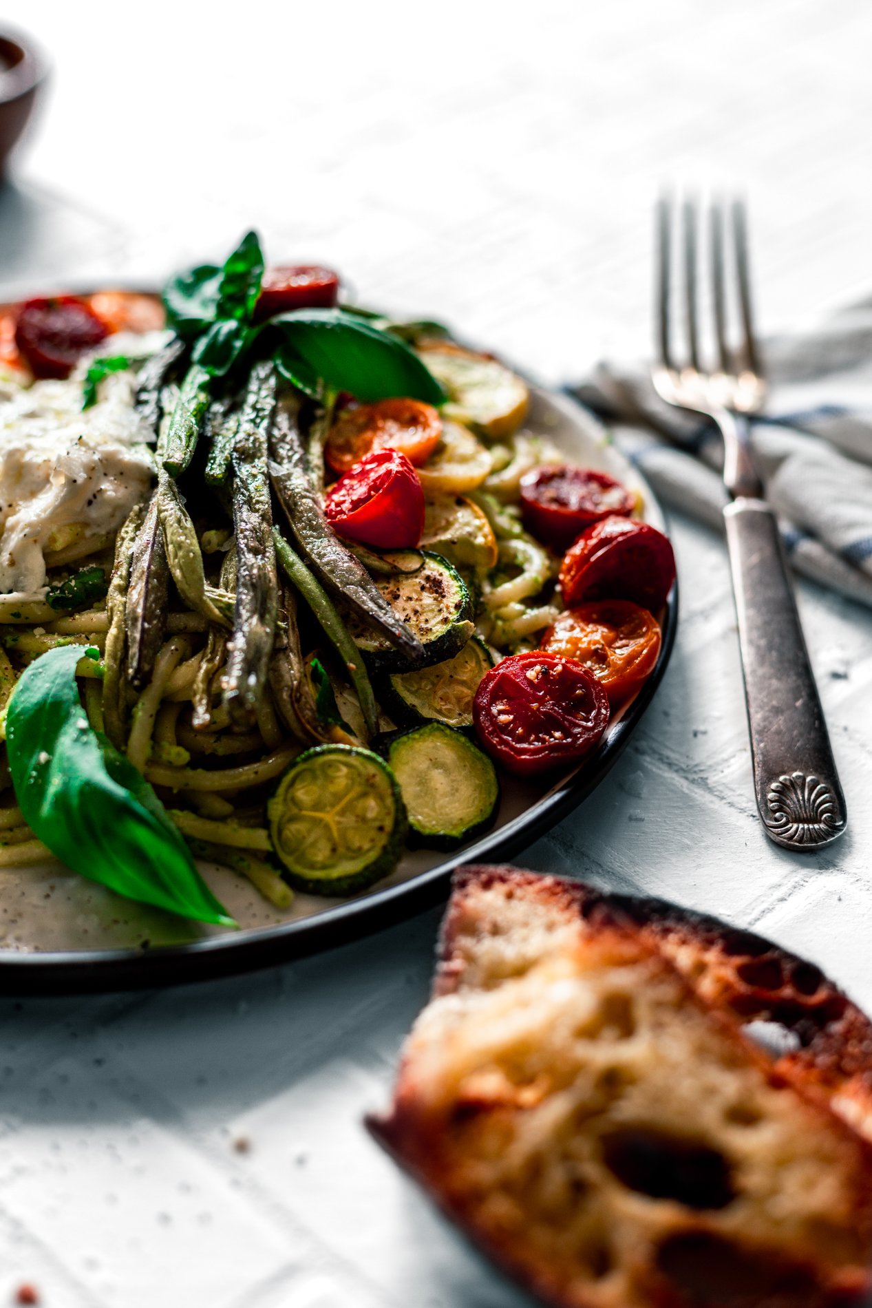 angled view of a plate of walnut pesto pasta with roasted summer vegetables