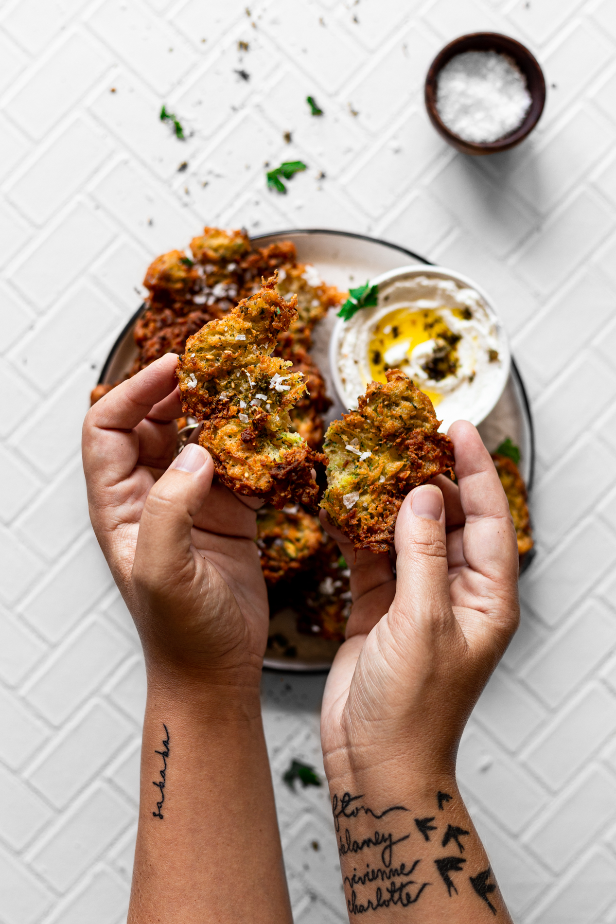overhead view of hands pulling apart a za'atar spiced zucchini fritter