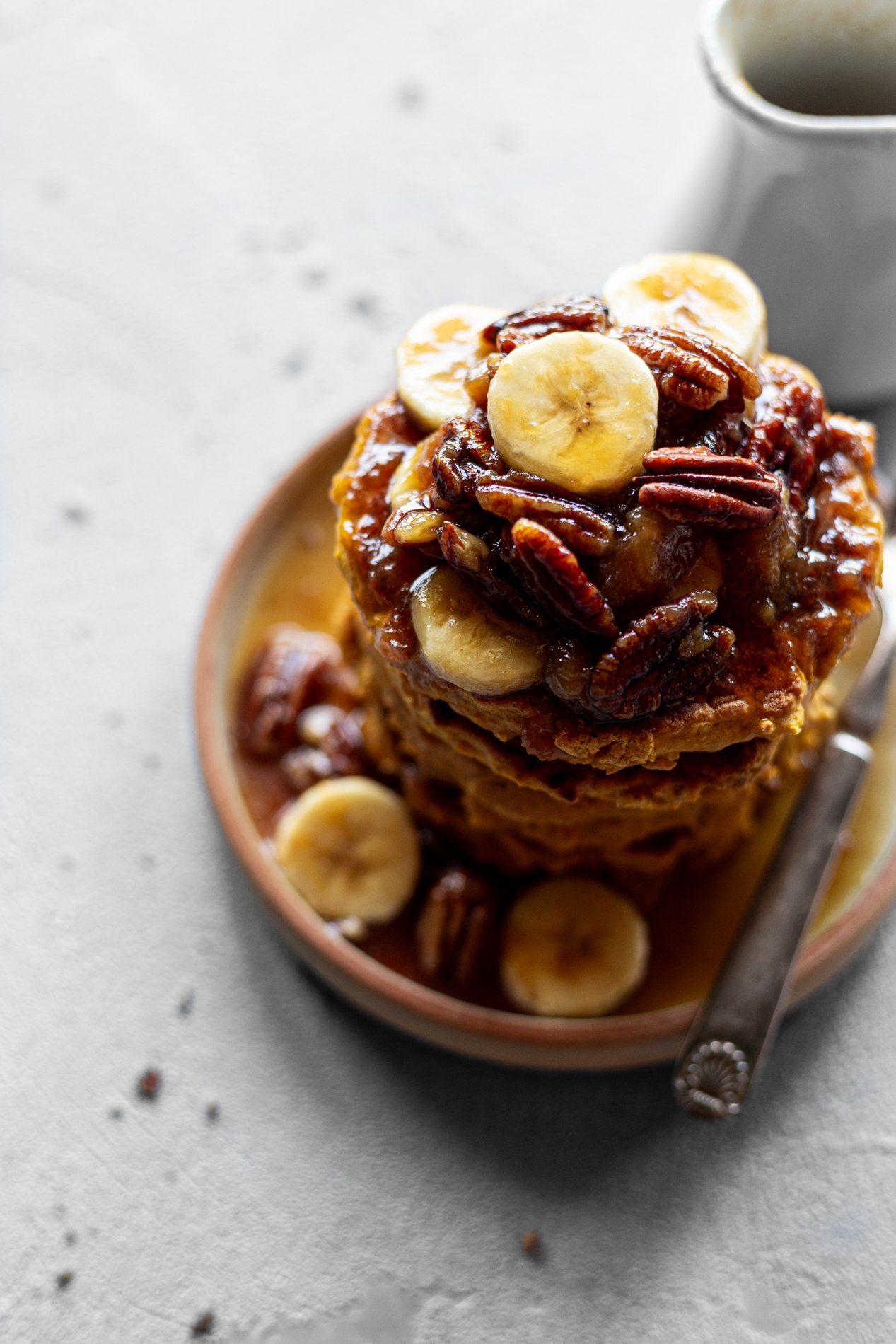 a stack of pumpkin break griddle cakes topped with caramelized bananas and pecans