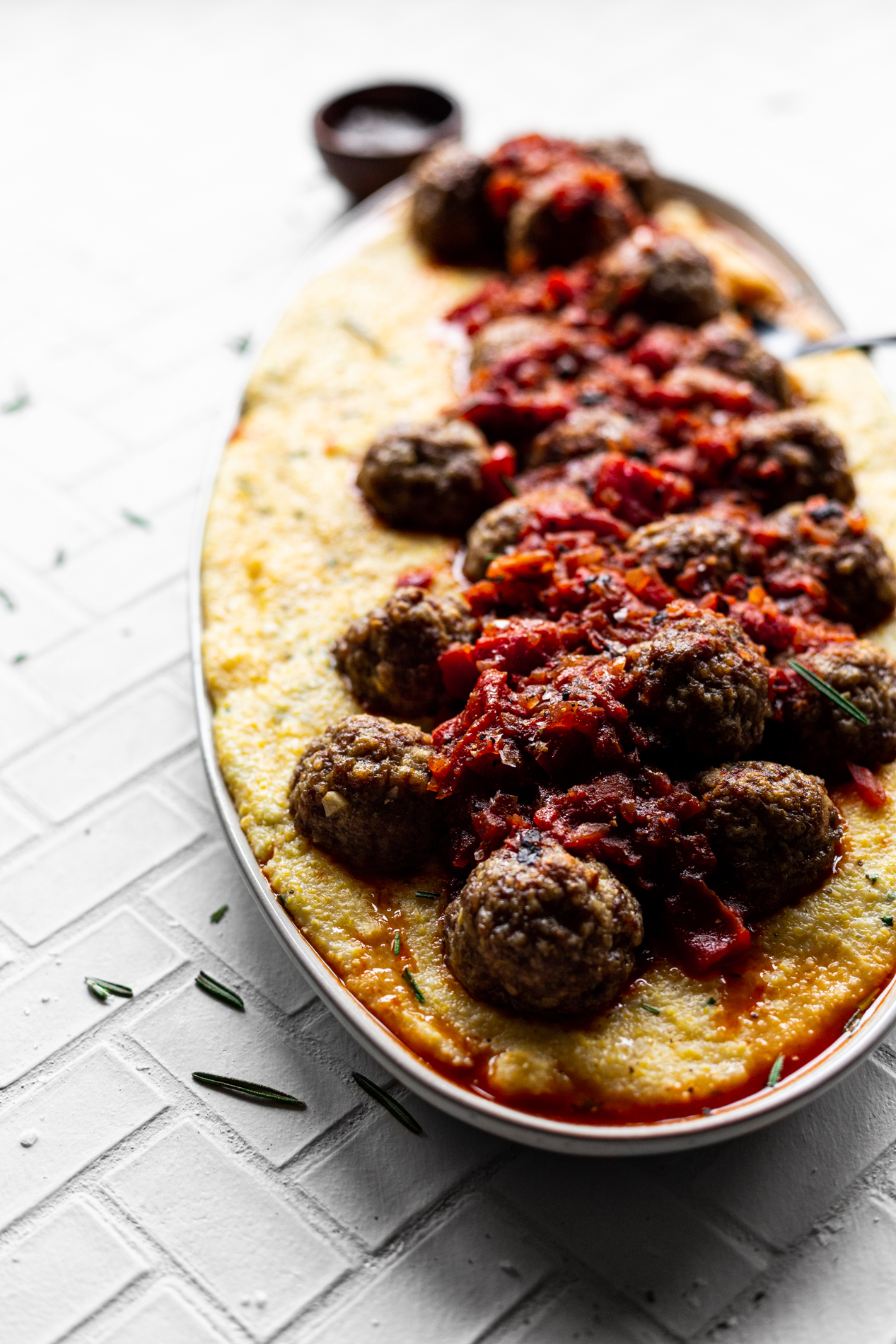 platter full of creamy polenta topped with lamb meatballs in a red pepper sauce