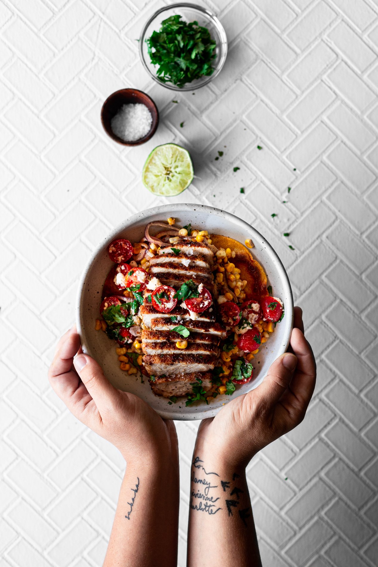 hands holding bowl of fajita spiced pork with mexican street corn and salsa