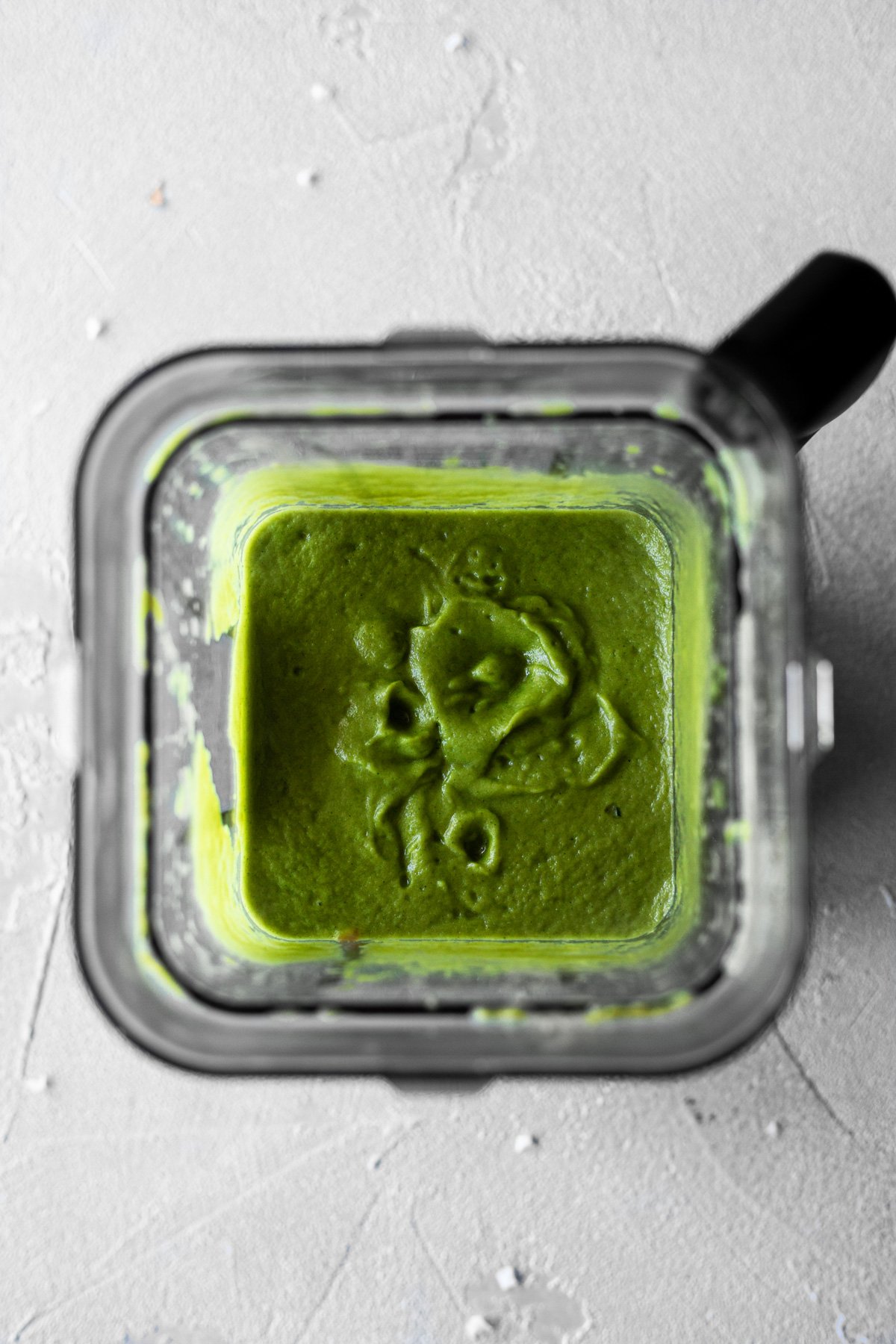 a high-powered blender filled with shallot, onion, poblano peppers, and zucchini after being blended