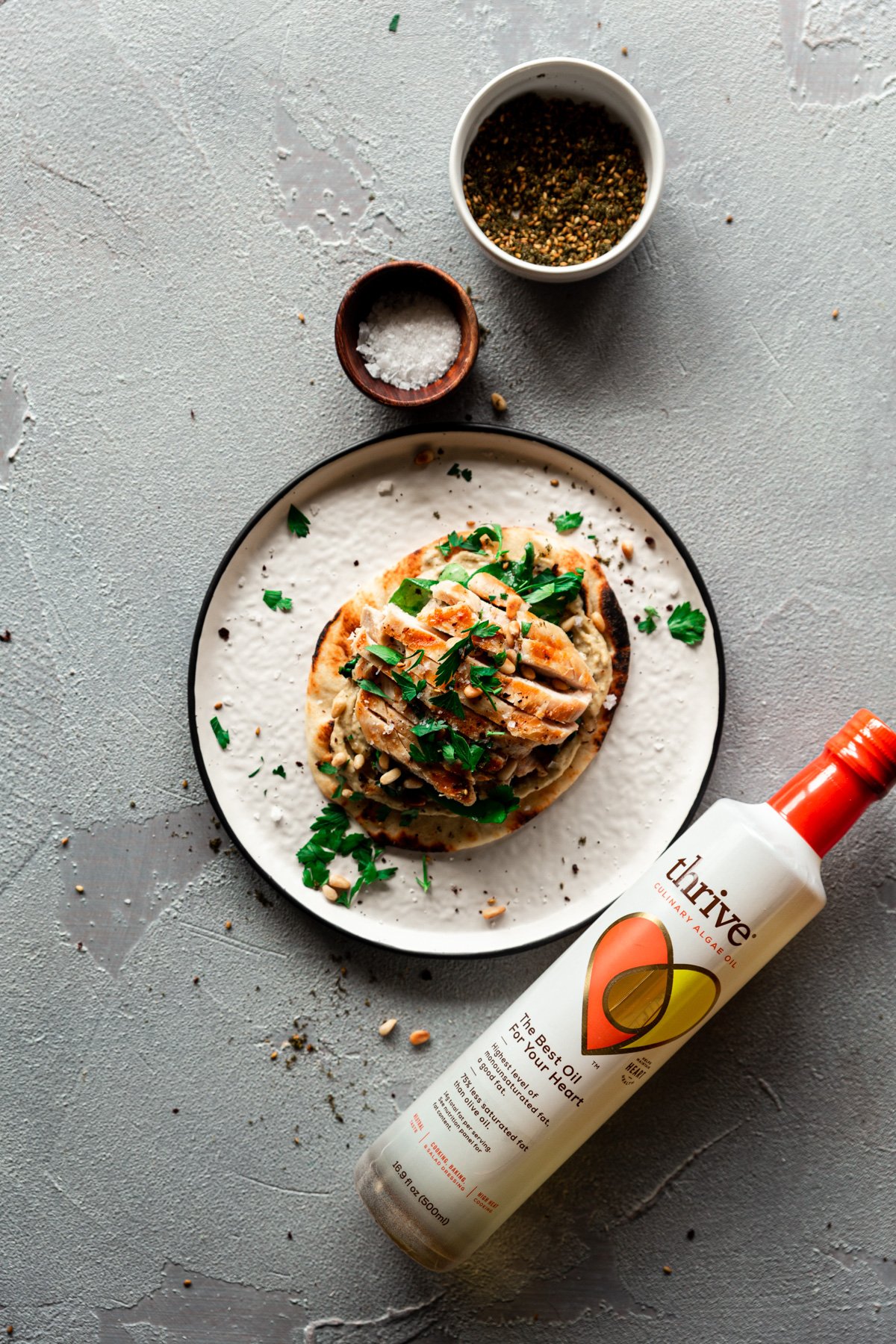 plate with grilled chicken flatbread with za'atar hummus and bottle of Thrive Algae Oil