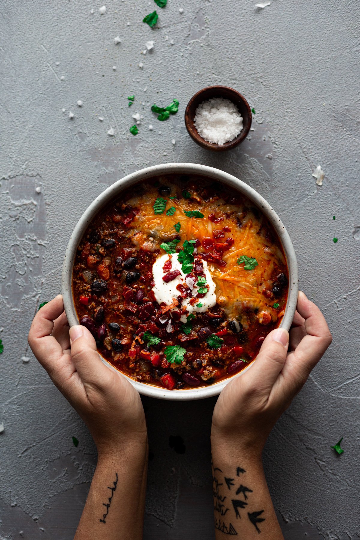 hands holding a bowl of the best chili recipe ever with cheese and sour cream