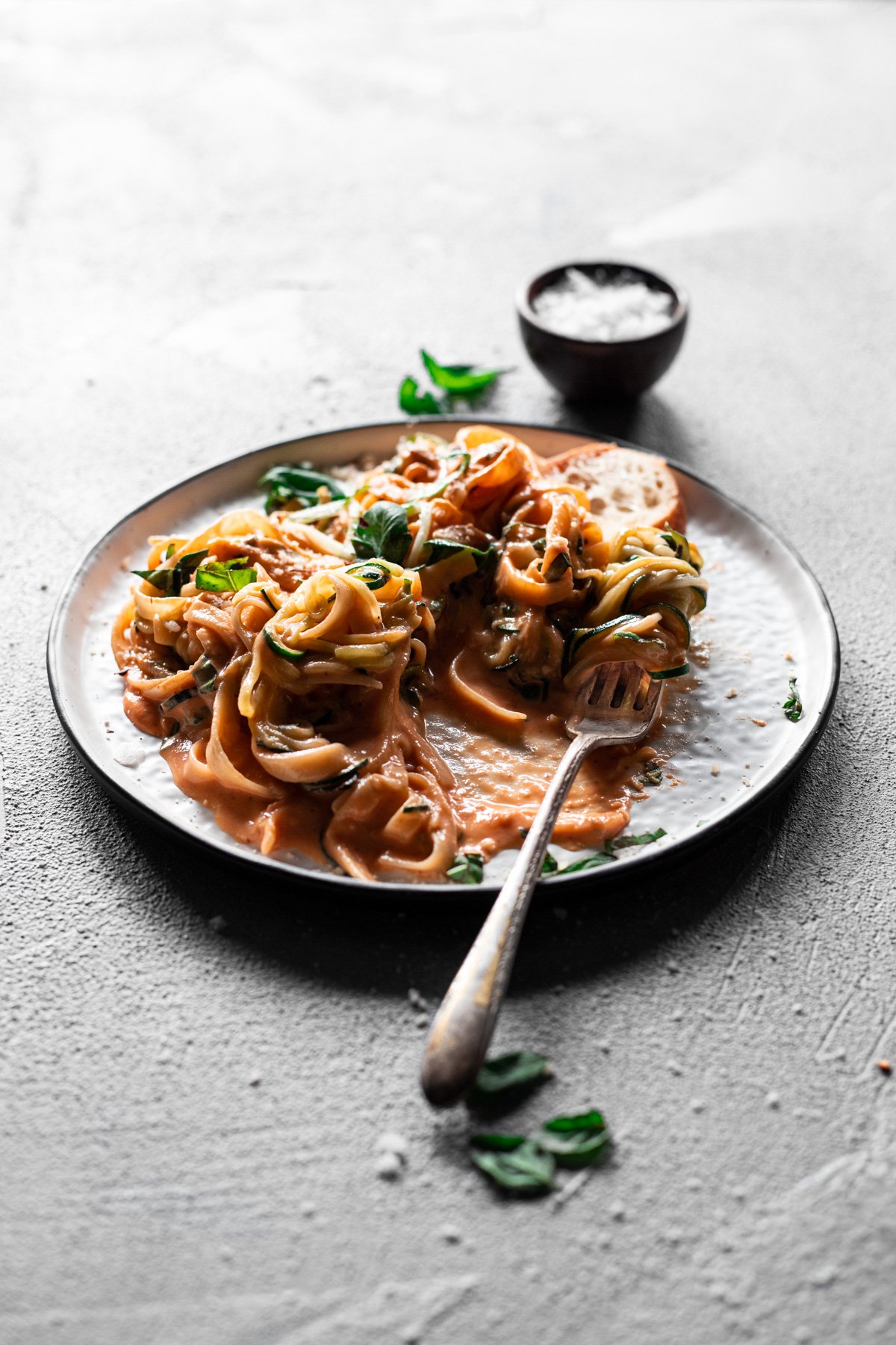 backlit plate of creamy roasted red pepper pasta with a fork