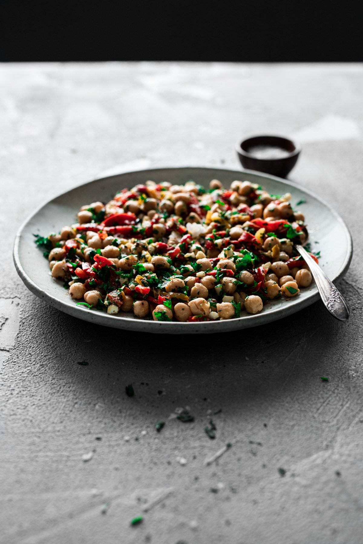 backlit platter with mediterranean chickpea salad recipe with serving spoon and bowl of sea salt