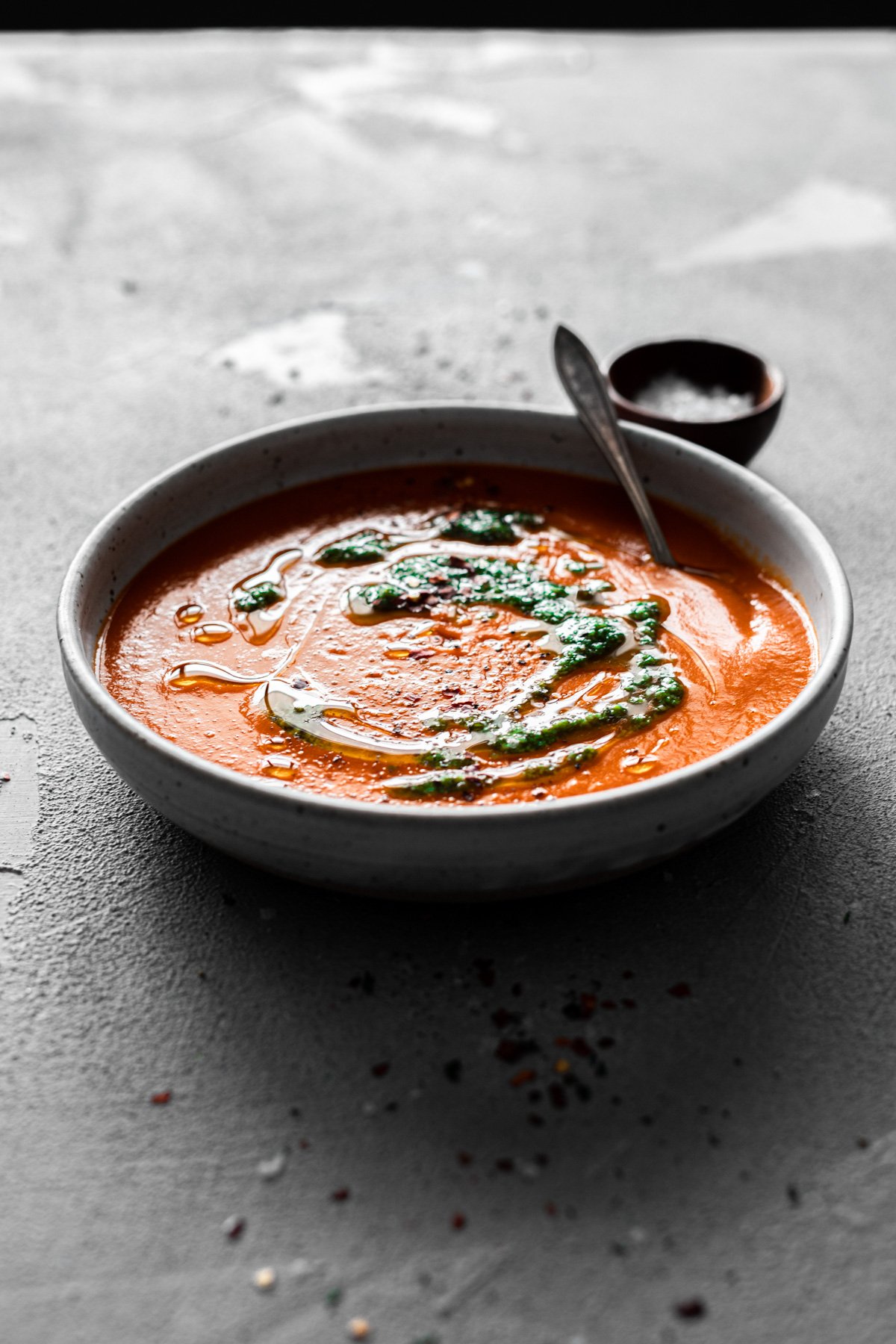 backlit bowl of roasted red pepper soup with pesto topping