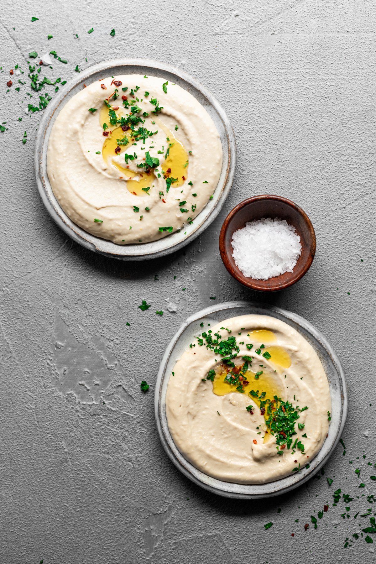 two dishes of creamy white bean hummus with olive oil and fresh parsley sprinkle